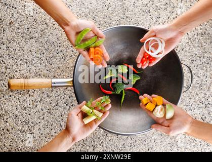 Quatre mains mettent les légumes frais dans le wok. Concept de cuisson Banque D'Images