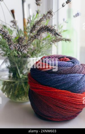 Boule de tissu de couleurs vives avec bouquet de lavande. Fil de laine coloré avec lavande dans le vase. Vie morte à l'aiguille. Passe-temps de tricot. Mode tricoté. Banque D'Images