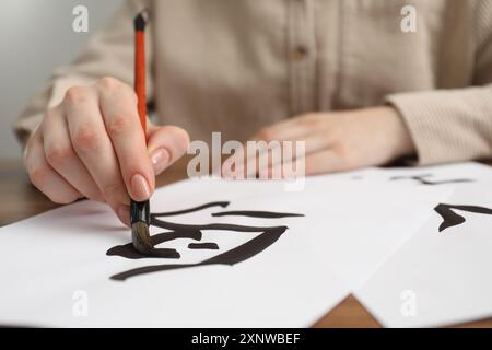 Calligraphie. Femme avec pinceau écrivant mot oiseau en chinois sur papier à table, gros plan Banque D'Images