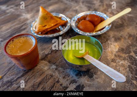 Un plateau de collations avec samosas, chutney, dessert sucré gulab jamun et kulhad chai, représentant un beau mélange de collations traditionnelles et de culture Banque D'Images