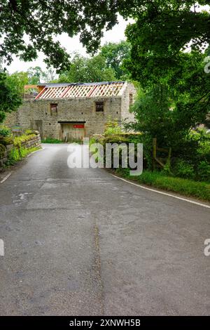 Une route de campagne sereine menant à un charmant bâtiment en pierre partiellement rénové entouré de verdure luxuriante. Banque D'Images