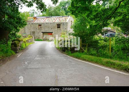 Pittoresque route de campagne mène à une vieille maison en pierre en cours de rénovation au milieu d'un cadre verdoyant luxuriant. Derbyshire Royaume-Uni. Banque D'Images