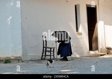 Une femme centenaire est assise sur une vieille chaise pour se reposer, un chat s'approche d'elle, monastère de Vracevsnica, Gornji Milanovac, Serbie centrale Banque D'Images