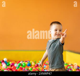 Joyeux garçon en bas âge souriant jouant dans une chambre d'enfants ou un centre de divertissement pour enfants avec des boules multicolores. Passe-temps actif heureux et enfance Banque D'Images