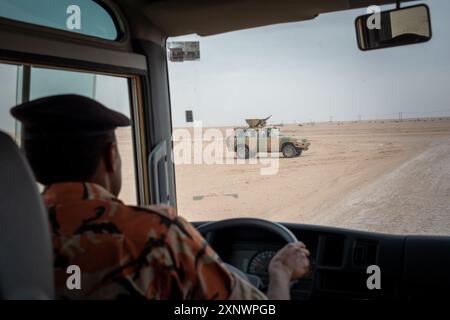 Image d'un véhicule militaire patrouillant dans le désert d'Oman, capturée de l'intérieur d'un autre véhicule. La scène véhicule des concepts de surveillance, de sécurité et de vigilance. Le vaste paysage vide met l'accent sur l'isolement et la vigilance. Banque D'Images