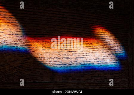La lumière colorée réfractée du soleil à travers le vitrail illumine les meubles à grains de chêne Banque D'Images