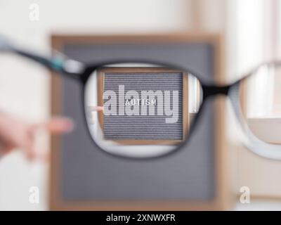 Kid points sur le papier à lettres gris avec le mot Autism. Vue à travers des lunettes sur le diagnostic médical qui habituellement fait dans l'enfance. Attirer l'attention sur de Banque D'Images