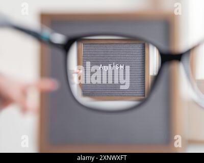Kid points sur le papier à lettres gris avec le mot Autism. Vue à travers des lunettes sur le diagnostic médical qui habituellement fait dans l'enfance. Attirer l'attention sur de Banque D'Images