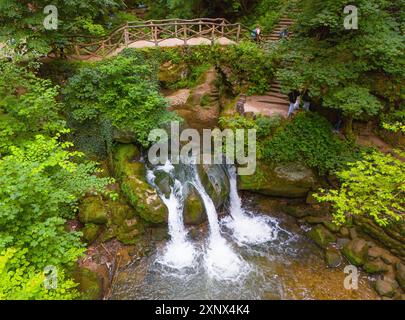 Une cascade coule à travers un paysage forestier verdoyant avec des rochers et un pont au-dessus, vue aérienne, cascade Schiessentuempel, Scheissendempel Banque D'Images