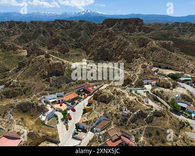 Village de montagne avec des maisons dispersées et paysage rocheux au premier plan, dans une vallée ensoleillée avec ciel clair et montagnes en arrière-plan Banque D'Images