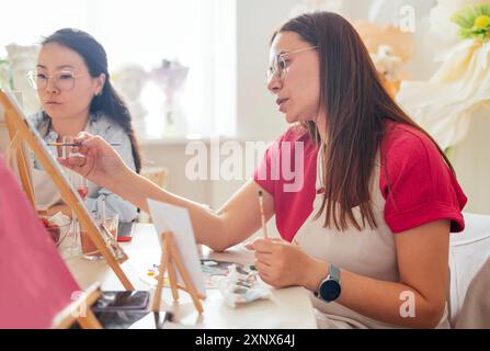 Gros plan de jeunes femmes en tenue décontractée dans un atelier de peinture. Amis à une table avec des chevalets et des toiles vierges. La vue de côté. Filles lea Banque D'Images