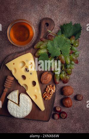 Fromage avec de grands trous, emmental, maasdam, fromage brie, sur une planche à découper, avec raisins et miel, noix, apéritif au vin, vue de dessus Banque D'Images
