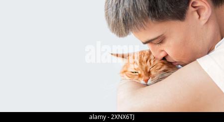 Gros plan portrait d'un homme caucasien câlin mignon chat au gingembre. Relation tendre avec l'animal moelleux et son maître. Copier l'espace sur fond blanc. Banque D'Images