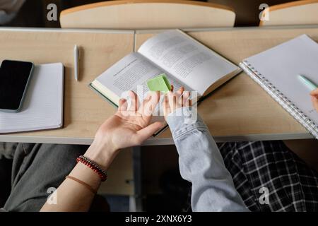 Image recadrée d'une étudiante qui passe une note papier à un camarade de classe pendant la classe universitaire. Les apprenants distraits remettent secrètement une feuille de berceau en classe, espace de copie Banque D'Images