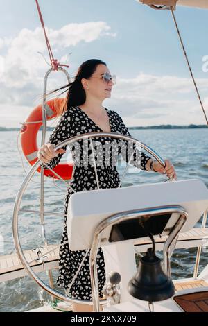 Une femme en lunettes de soleil et une robe noire et blanche dirigeant un bateau par une journée ensoleillée avec des eaux calmes et un sauveteur en arrière-plan. Bélarus Banque D'Images