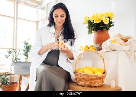 Portrait de mains féminines bien entretenues tient le citron et le couteau. Jeune femme en robe et chemise épluche les agrumes. Fille brune avec manucure soignée naturelle Banque D'Images