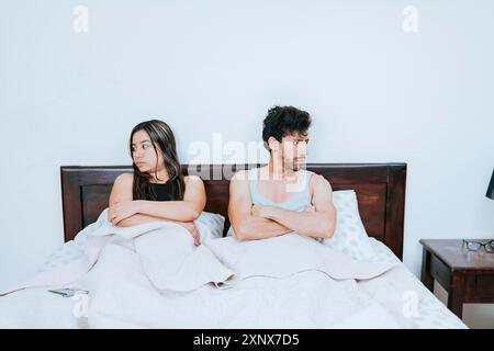 Couple conflictuel assis sur le lit, couple contrarié assis sur le lit avec les bras croisés. Jeune couple se disputant assis dans le lit, couple contrarié assis sur le lit Banque D'Images