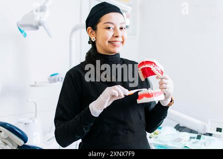 Dentiste souriante montrant une prothèse dentaire, dentiste expliquant le brossage des dents, dentiste féminine montrant une prothèse dentaire et une brosse Banque D'Images