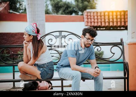 Couple malheureux assis dos à dos sur le banc. Concept de problèmes de couple et de crise. Jeune couple bouleversé assis dos à dos dans un parc, jeune couple Banque D'Images