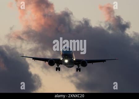 Avion volant dans le ciel bleu avec des nuages au coucher du soleil. Banque D'Images