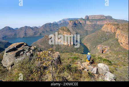 Jeune homme debout sur un rocher dans un paysage de canyon, coude de rivière à Blyde River Canyon avec trois Rondawels pic, vue sur le canyon avec Blyde River et Banque D'Images