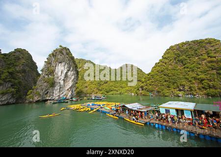 Les vacanciers font la queue pour un kayak sur une jetée, derrière les rochers karstiques dans la baie de LAN Ha, baie d'Halong, Vietnam Banque D'Images