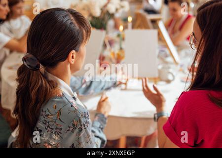 Gros plan de jeunes femmes en tenue décontractée dans un atelier de peinture. Amis à une table avec des chevalets et des toiles vierges. La vue de l'arrière. Filles lea Banque D'Images