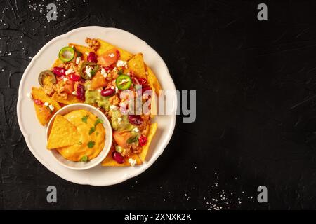 Nachos chargés avec Chili con carne, guacamole et salsa au fromage, filés depuis le haut sur un fond sombre avec espace de copie Banque D'Images