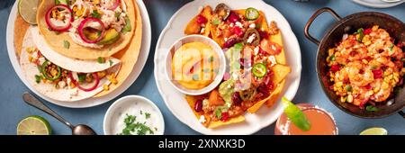 En-tête panoramique cuisine mexicaine sur fond bleu. Nachos au piment con carne, tacos au poulet, et diverses sauces, top shot Banque D'Images