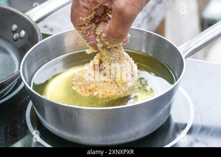 Main mettant soigneusement un morceau de poulet pané dans une casserole avec de l'huile bouillante pour la friture, concept de cuisson, foyer sélectionné, profondeur de champ étroite Banque D'Images