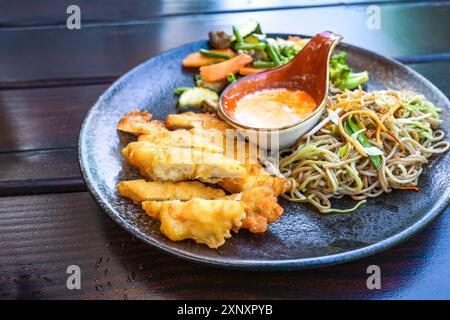 Filet de poulet pané avec nouilles frites, légumes et sauce au curry à la noix de coco, cuisine asiatique sur une table en bois foncé, foyer sélectionné, profondeur étroite Banque D'Images