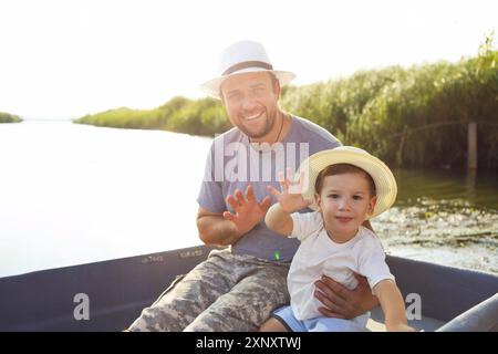 Joyeux père embrassant un petit garçon mignon et se foulant les mains en bateau pendant la pêche le jour ensoleillé de l'été Banque D'Images