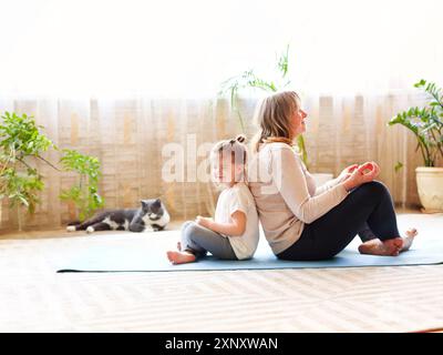 Femme mature et petite fille assise sur un tapis dans lotus poser et méditer tout en faisant du yoga dans la chambre spacieuse à la maison ensemble Banque D'Images