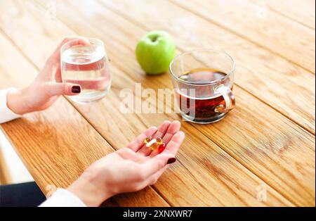 Angle élevé de la femelle anonyme avec des pilules et une tasse d'eau en mélange à table avec du thé et de la pomme pendant la maladie Banque D'Images