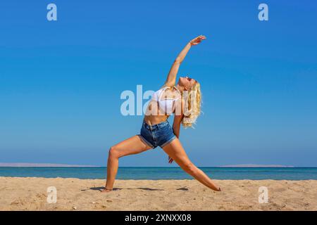 Jeune femme caucasienne blonde formant yoga sur la plage près de la mer Banque D'Images