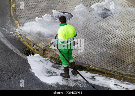 L'employé qui tient un tuyau nettoie le trottoir avec de l'eau et du détergent. Concept d'entretien ou de nettoyage Banque D'Images