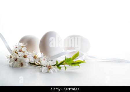 Trois oeufs blancs de Pâques avec une petite branche de fleurs de fruits sauvages sur un fond clair avec espace de copie, foyer sélectionné, profondeur de champ étroite Banque D'Images