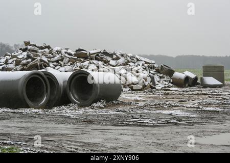 Tuyaux en béton cassés et nouveaux pour l'installation de drainage sur un chantier de construction dans le champ sur une journée humide et enneigée, objectif sélectionné, profondeur étroite de Banque D'Images