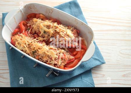 Poivrons pointus farcis avec riz, thon, tomates et fromage cuits dans une cocotte fraîchement sortie du four, serviette bleue et bois peint blanc Banque D'Images