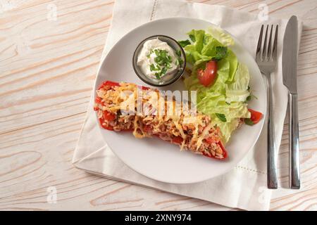 Poivron demi-pointu cuit avec du riz, du thon, des tomates et du fromage sur une assiette blanche avec salade de laitue et tremper sur du bois peint blanc, copier l'espace Banque D'Images