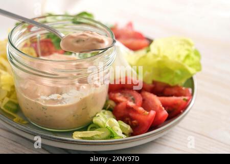 Vinaigrette à salade de skyr sur une cuillère et dans un pot en verre sur une assiette avec des tranches de laitue et de tomates, repas cru sain, foyer sélectionné, étroit Banque D'Images