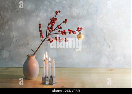 Minimaliste troisième avènement avec quatre petites bougies, trois brûlent et une branche de baies avec une boule de noël dorée dans un vase, fond enneigé avec Banque D'Images