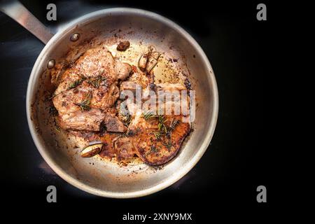 Côtelettes de porc rôties avec des herbes, des épices et de l'ail dans une poêle sur une table de cuisson noire, concept de nourriture et de cuisson, espace de copie, vue de dessus Banque D'Images