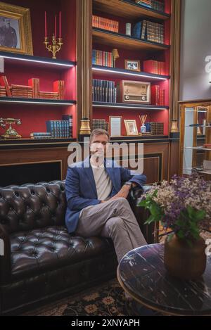 Homme assis sur un canapé en cuir luxueux dans une bibliothèque opulente avec décor Vintage Banque D'Images