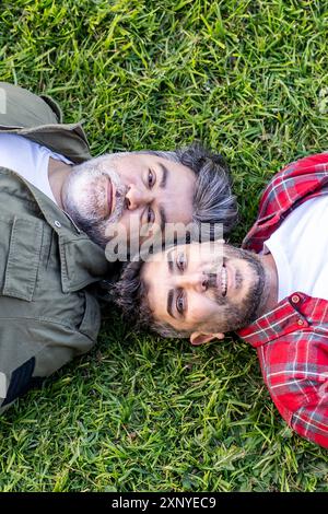 Vue de dessus d'un couple gay hispanique allongé sur l'herbe en regardant la caméra. Prise de vue verticale Banque D'Images