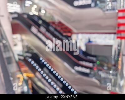 Arrière-plan flou avec des gens en mouvement sur les escaliers mécaniques à l'intérieur d'un centre commercial moderne. Vue intérieure du centre commercial défocalisé Banque D'Images