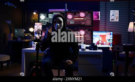 Pirate informatique dissimulant une identité filmant une vidéo de rançon dans une base souterraine cachée, menaçant de divulguer publiquement des données volées si les demandes de paiement ne sont pas satisfaites, utilisant le téléphone pour enregistrer des images de chantage, caméra B. Banque D'Images