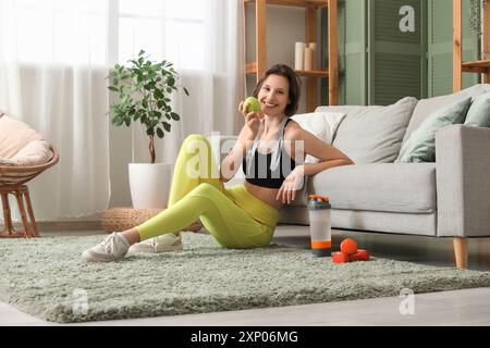 Belle jeune femme heureuse avec ruban à mesurer, bouteille d'eau et pomme fraîche assis à la maison. Concept de perte de poids Banque D'Images