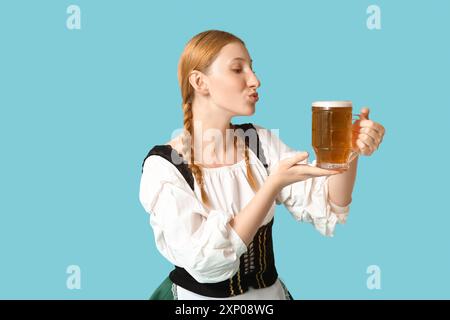 Belle serveuse Octoberfest heureuse avec tasse de baiser soufflant de la bière sur fond bleu Banque D'Images