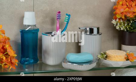 Vue rapprochée de l'étagère de salle de bain en verre avec bouteille de rinçage vocal, brosse à dents, savon, éponges de douche et fleurs Banque D'Images